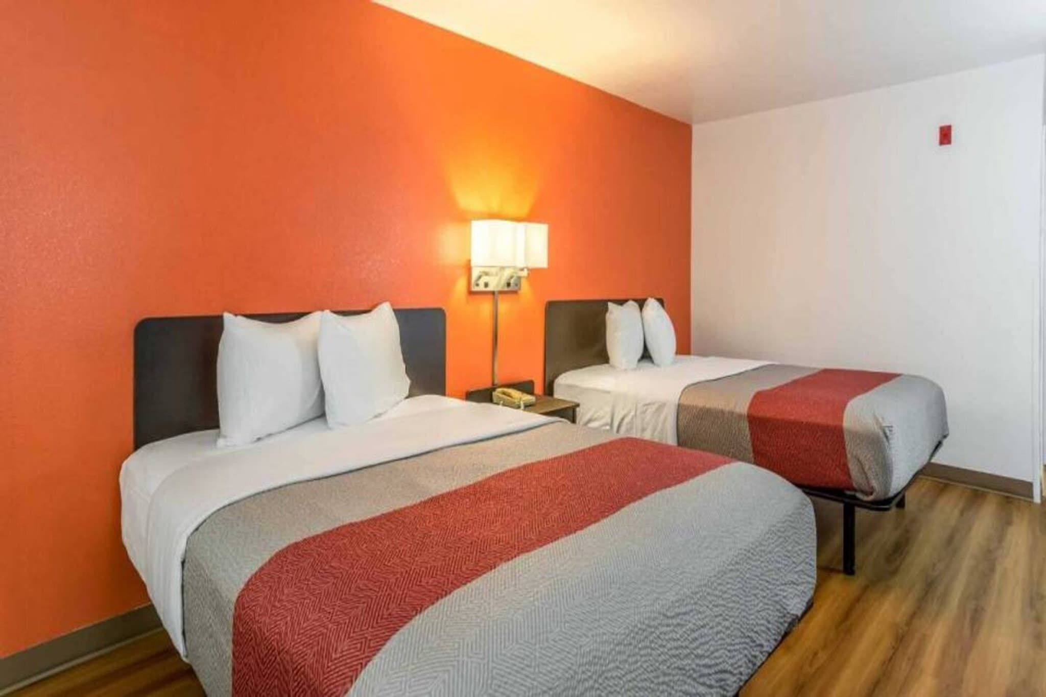 A hotel room with two beds, a nightstand, a lamp, and a red wall.