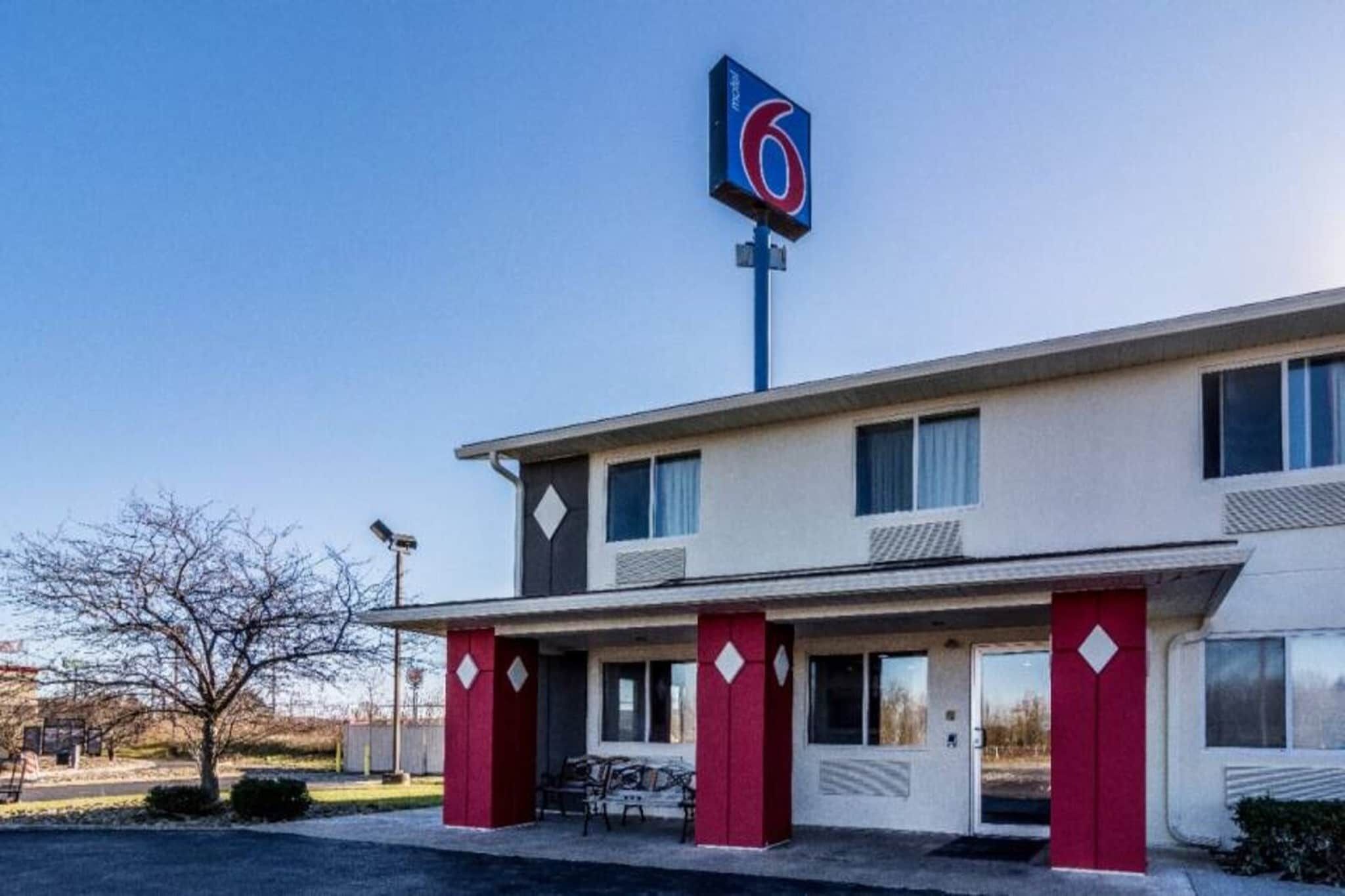 A motel with a prominent '6' sign, a flat roof, and a simple facade with a red door and windows.