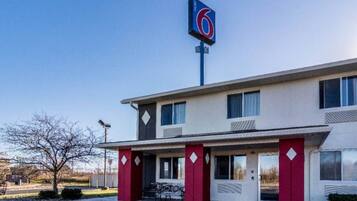 A motel with a prominent '6' sign, a flat roof, and a simple facade with a red door and windows.