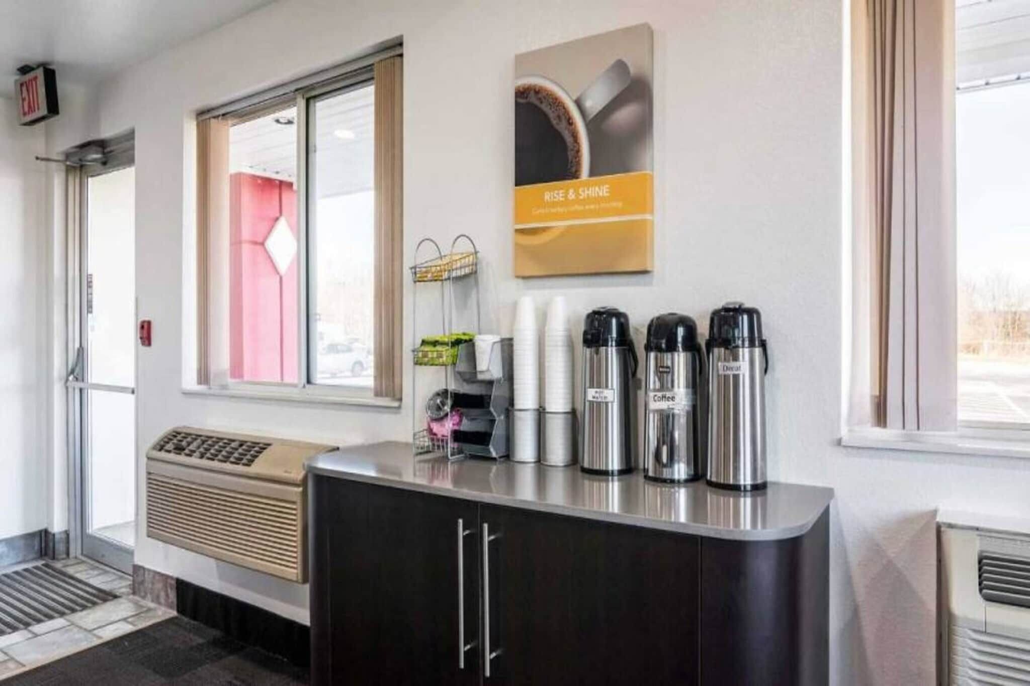 Uma área de recepção de hotel com um canto de café, uma placa na parede e uma janela com vista.