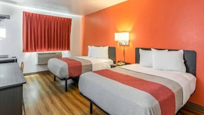 Une chambre d’hôtel avec deux lits, un bureau et une fenêtre avec des rideaux rouges.