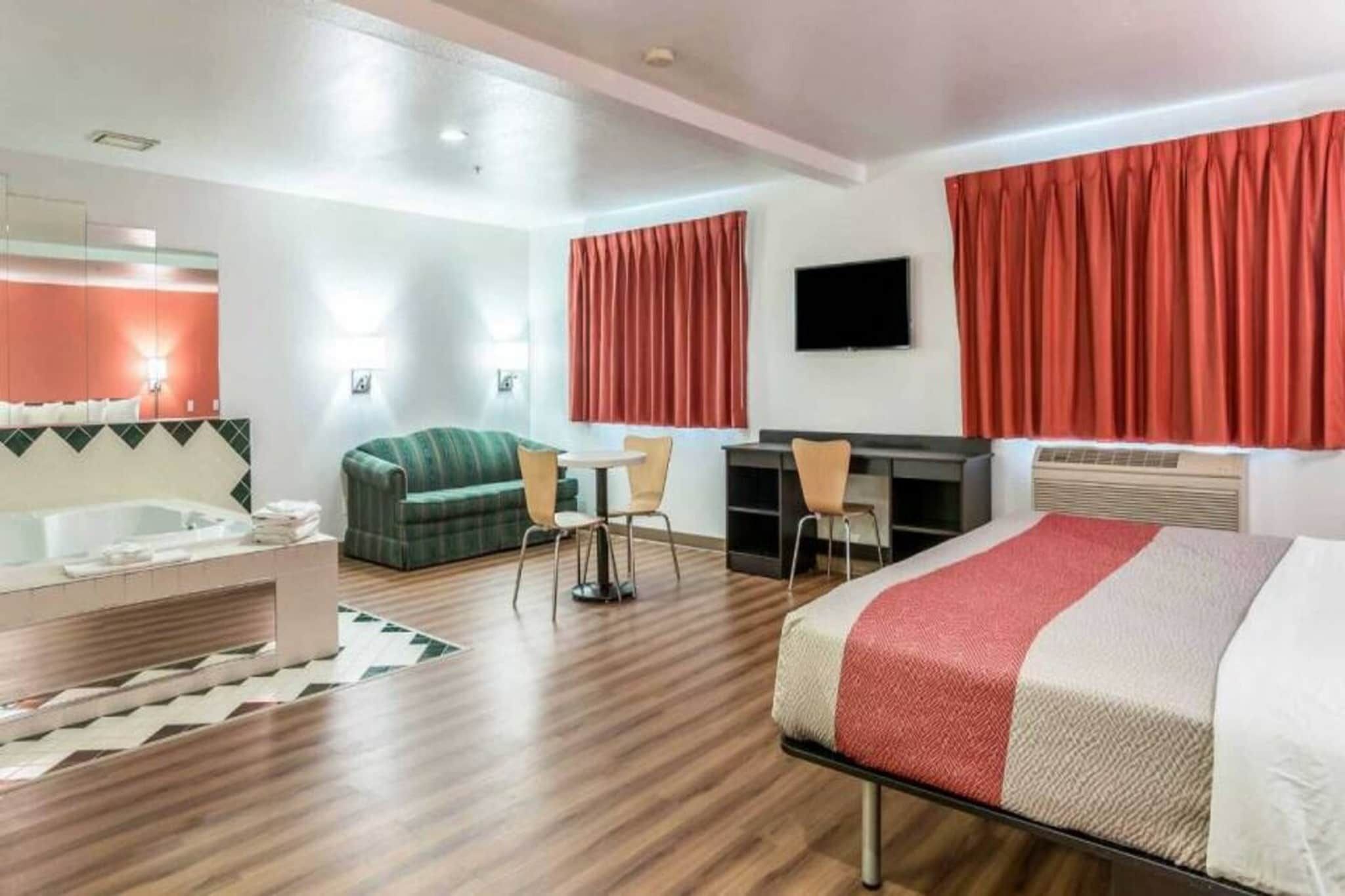 A hotel room with a bed, a desk, a chair, a sofa, a TV, and a bathroom.