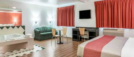 A hotel room with a bed, a desk, a chair, a sofa, a TV, and a bathroom.