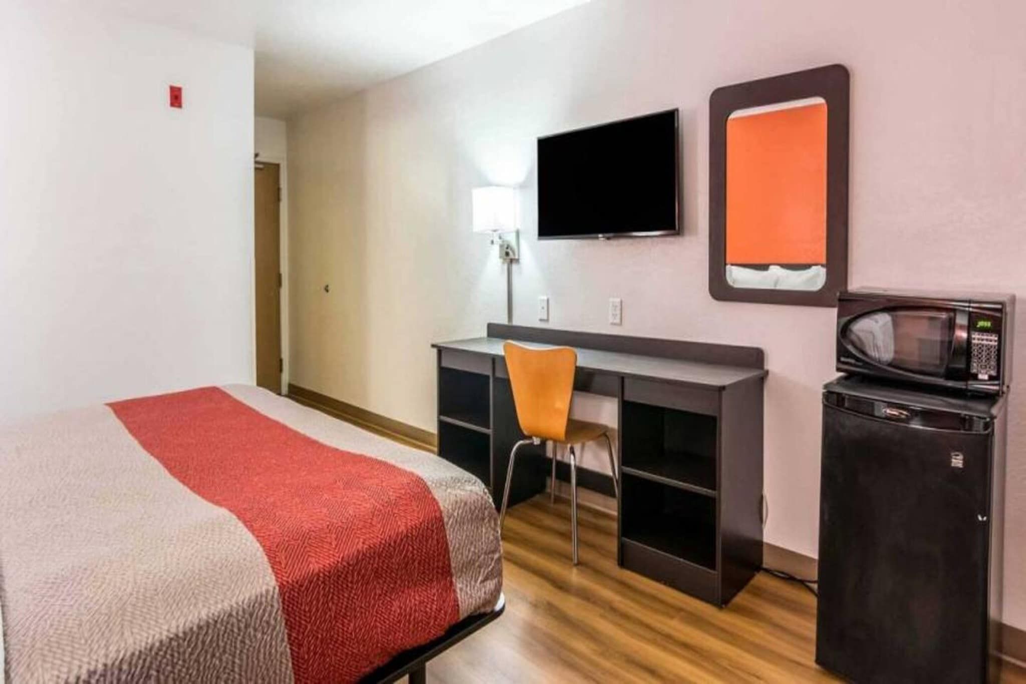 A hotel room with a bed, a desk, a chair, a television, and a microwave.