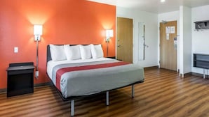Een hotelkamer met een bed, nachtkastje, bureau, kledingkast en spiegel.