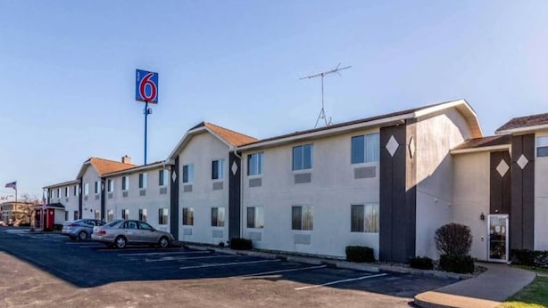 Een motel met een opvallend bord met het cijfer '6', een parkeerplaats en een rij laagbouwgebouwen met een eenvoudig ontwerp.