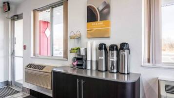 A hotel reception area with a coffee station, a wall-mounted sign, and a window with a view.