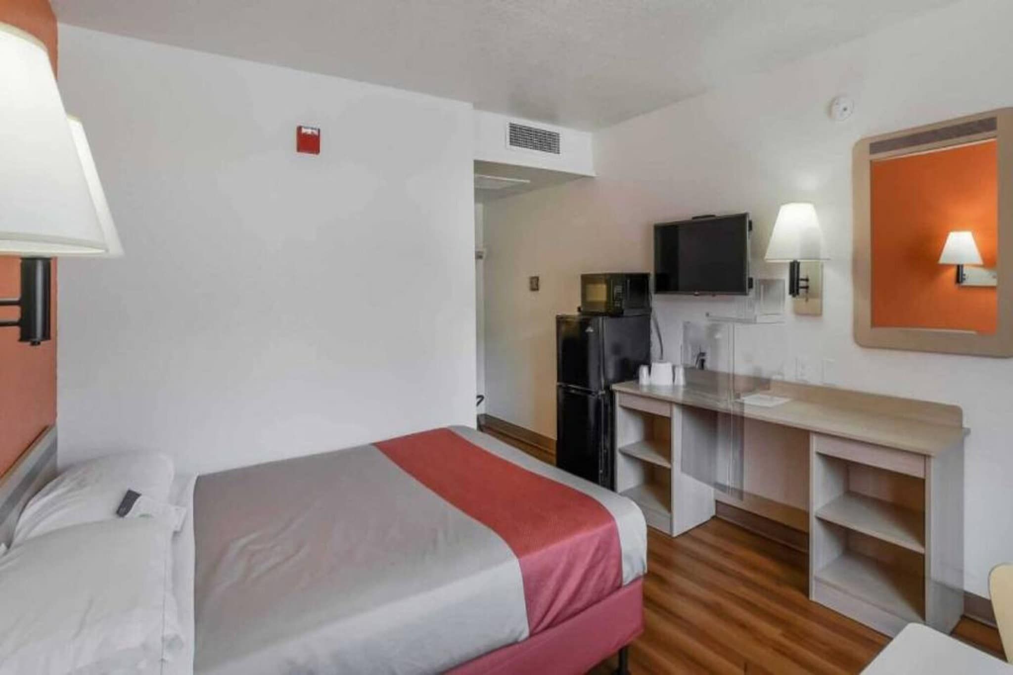 A hotel room with a bed, a desk, a television, and a kitchenette.