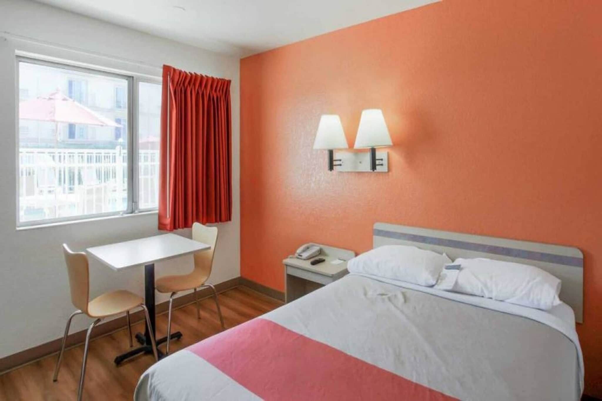 Ett hotellrum med en säng, ett skrivbord, en stol, ett nattduksbord och ett fönster med gardiner.