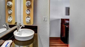 A bathroom with a sink, mirror, towel dispenser, and a separate kitchenette area with a stove. - ADA Full Bed | RI Shower (Medford OR)