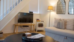 A living room with a TV on a stand, a small heater, a sofa, and a lamp. - Malvern Hills 3-Bed Retreat | Sleeps 8 | Free Park (Worcestershire)