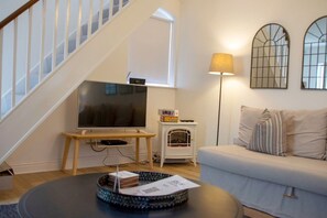 Una sala de estar con una televisión sobre un mueble bajo, un calentador pequeño, un sofá y una lámpara.