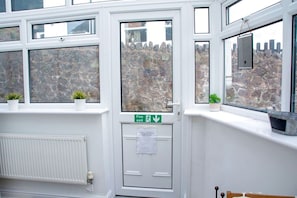 Une porte blanche avec un panneau indiquant la sortie de secours, un radiateur et des plantes en pot sur les rebords des fenêtres.