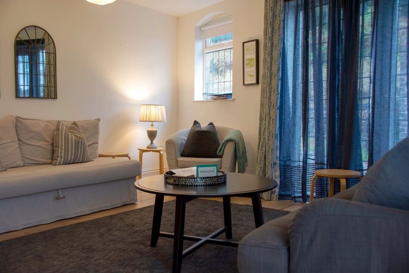 A living room with a sofa, a coffee table, a lamp, and a window with curtains.