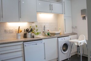 Una cocina moderna con armarios blancos, lavavajillas, lavadora y una trona para bebé.