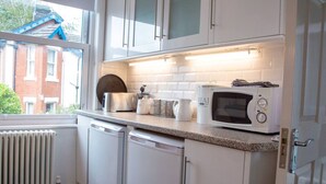A kitchen with white cabinets, a microwave, a toaster, and a kettle on the countertop. - Malvern Hills 3-Bed Retreat | Sleeps 8 | Free Park (Worcestershire)