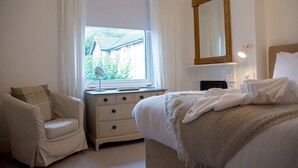 A bedroom with a bed, a chair, a dresser, a mirror, and a window with curtains. - Malvern Hills 3-Bed Retreat | Sleeps 8 | Free Park (Worcestershire)