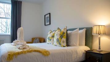 Una camera d'albergo con un letto, cuscini, una lampada da comodino, una finestra con tende e un termosifone.