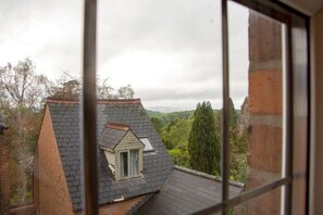 Une vue à travers la fenêtre d’un bâtiment doté d’un toit en pente, d’une petite fenêtre de grenier et d’un mur en briques.