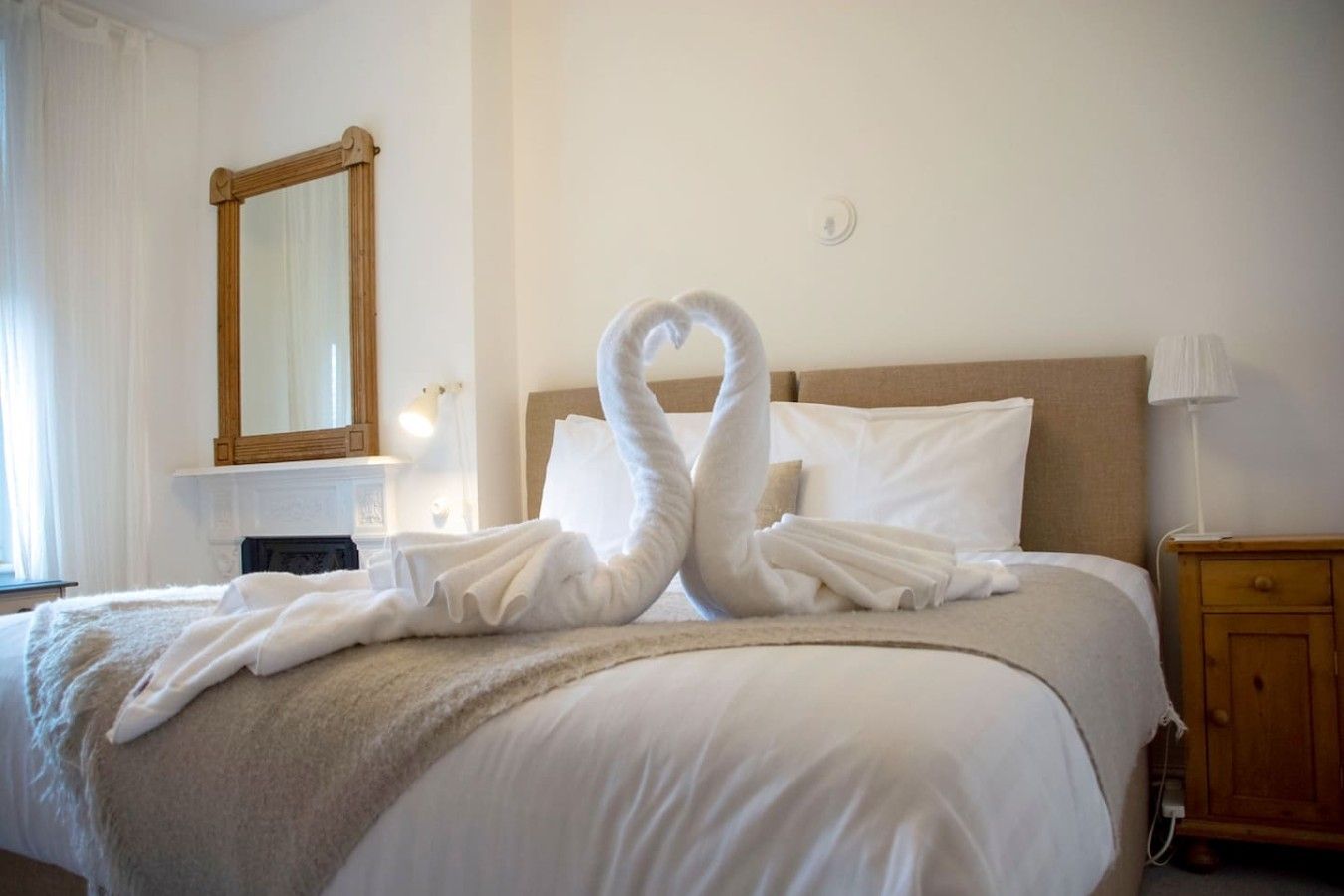 Een hotelkamer met een bed, een houten nachtkastje, een spiegel en een lamp.