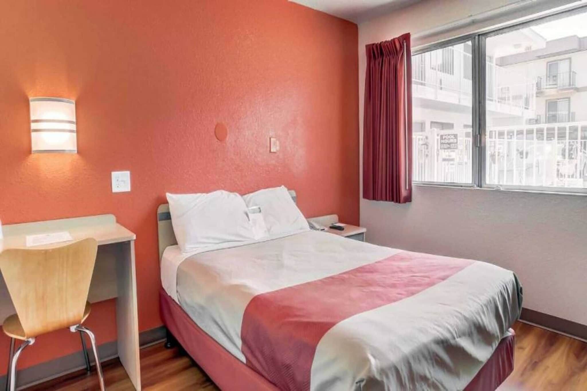 A hotel room with a bed, a desk, a chair, a window with curtains, and a view of the outside.