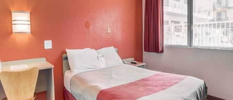 Une chambre d’hôtel avec un lit, un bureau, une chaise, une fenêtre avec des rideaux et une vue sur l’extérieur.