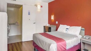 A hotel room with a bed, bedside table, and a bathroom door. - 1 Full Bed | ADA/Tub (Medford OR)