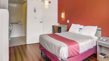 Una habitación de hotel con cama, mesita de noche y puerta de baño.