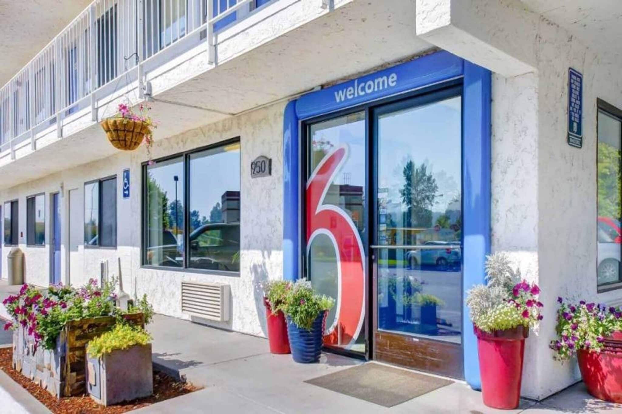 A hotel entrance with a large '6' sign, a 'welcome' sign above the door, and potted plants in front.