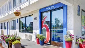 Entrada de hotel con un gran letrero con el número '6', un cartel de 'bienvenida' sobre la puerta y plantas en macetas al frente.