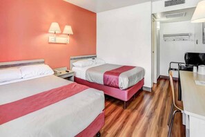 Een hotelkamer met twee bedden, een bureau en een kitchenette.