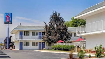 Ein Motel mit blauem Schild, einem Parkplatz und einem Baum davor.