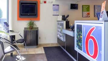 Ein Hotel-Rezeptionsbereich mit einer Rezeption, einem an der Wand befestigten Fernseher und einem großen Schild mit der Zahl 6.