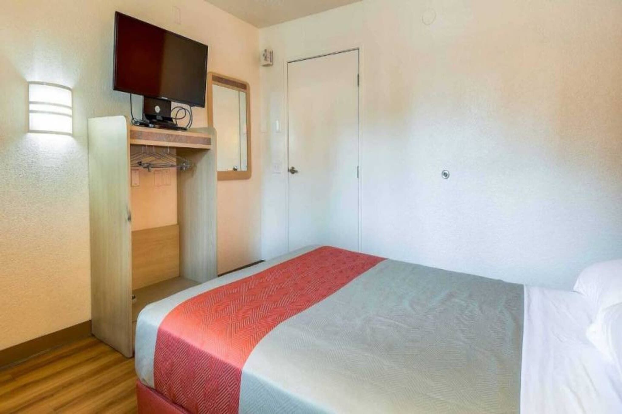 Una habitación de hotel con una cama, un televisor fijado en la pared y una puerta.