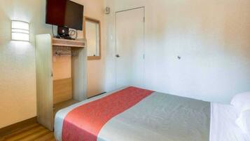 Una habitación de hotel con una cama, un televisor fijado en la pared y una puerta.