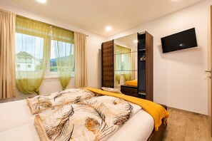 A bedroom with a bed, a TV, a wardrobe, and a window with curtains. - Vrbo Property (St. Michael Bleiburg)