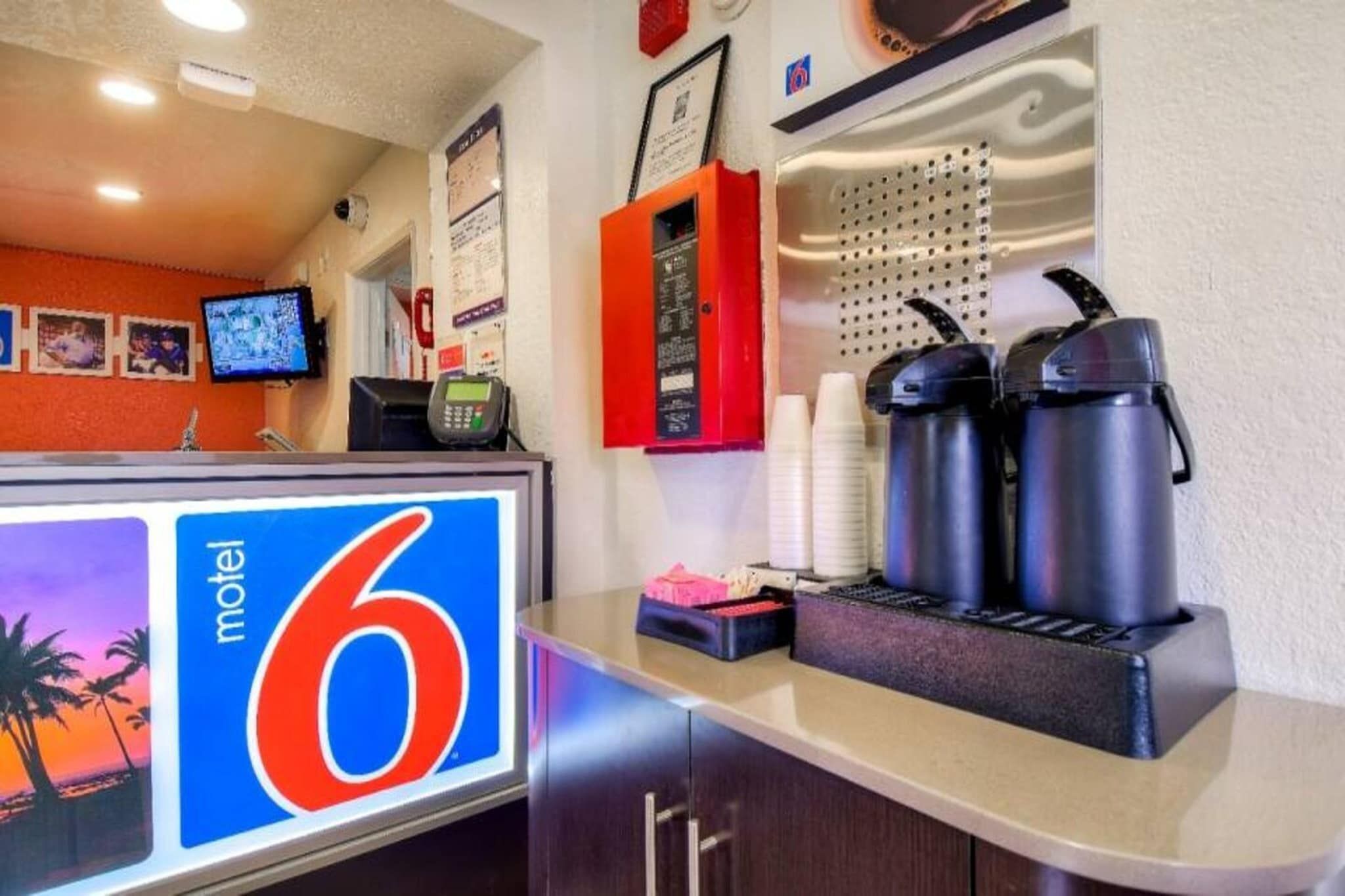 A motel reception desk with a large sign, a coffee station, and a monitor displaying a tropical scene.