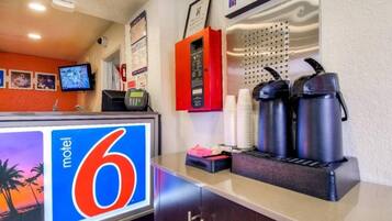 A motel reception desk with a large sign, a coffee station, and a monitor displaying a tropical scene.