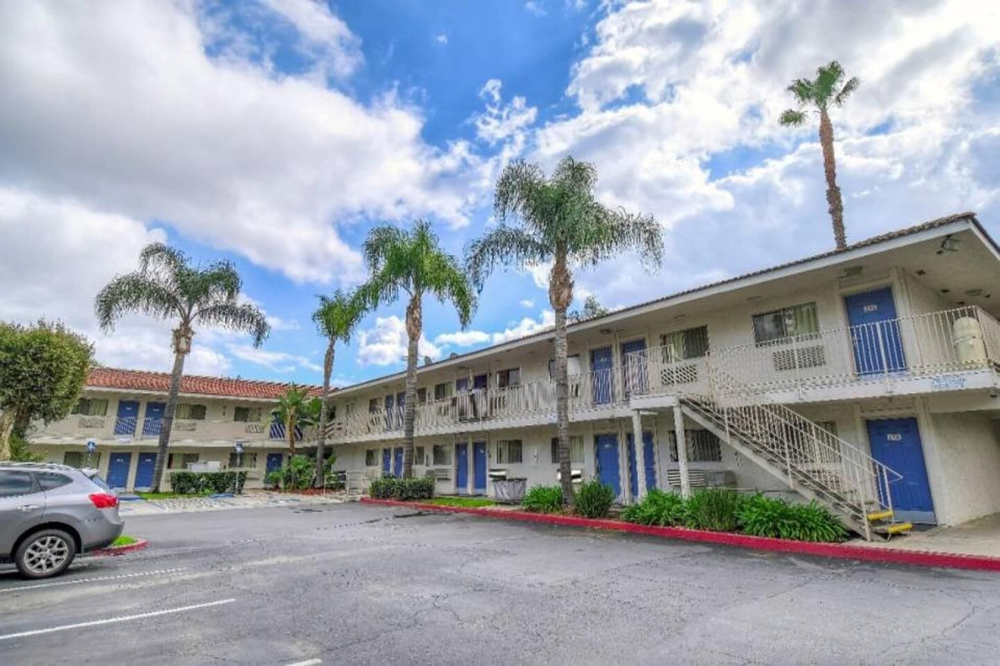 A motel with multiple-story buildings, a parking lot, and palm trees.