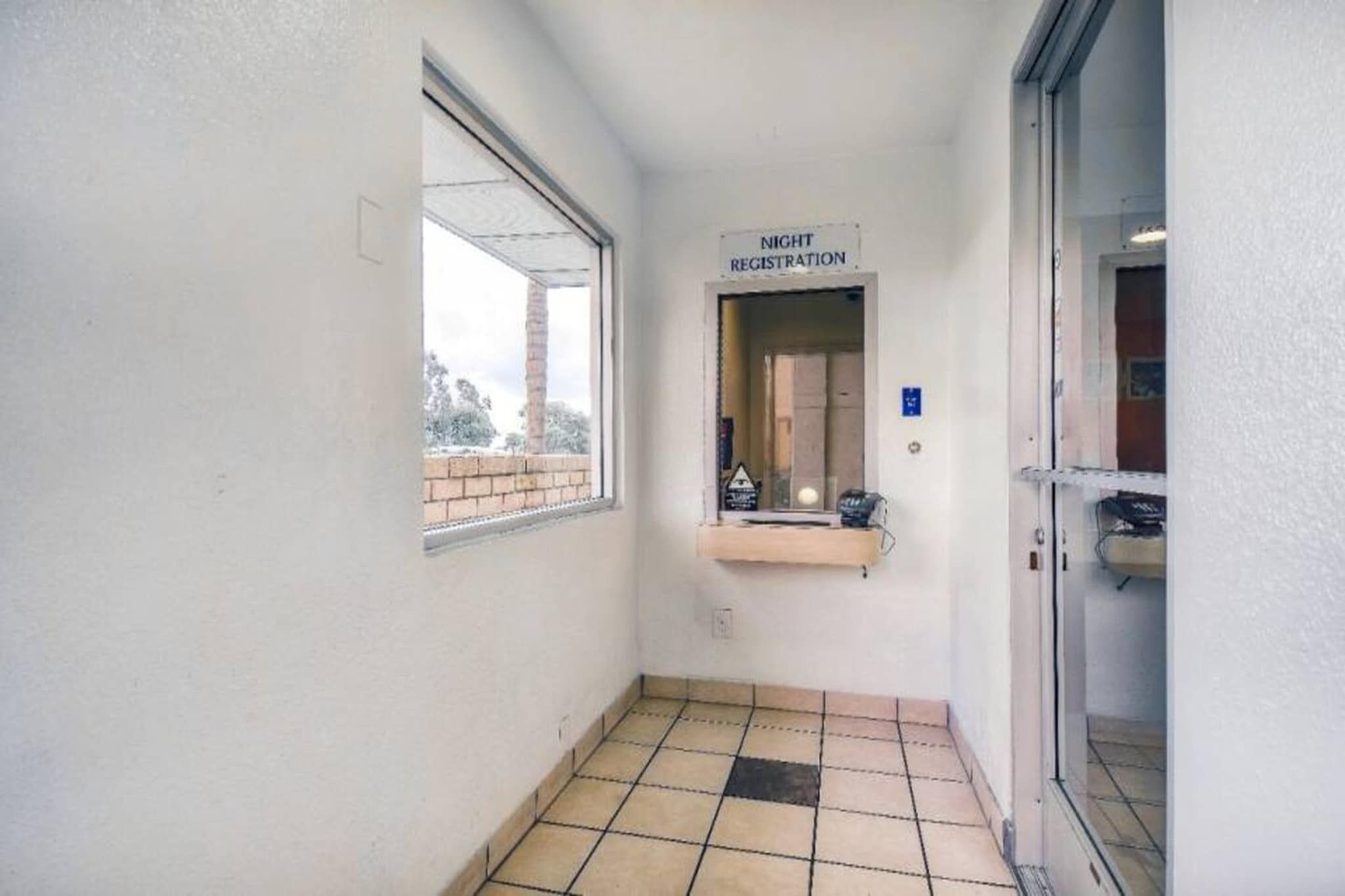 A narrow hallway with a window on the left and a door on the right. There is a sign above the door that reads 'NIGHT REGISTRATION'.