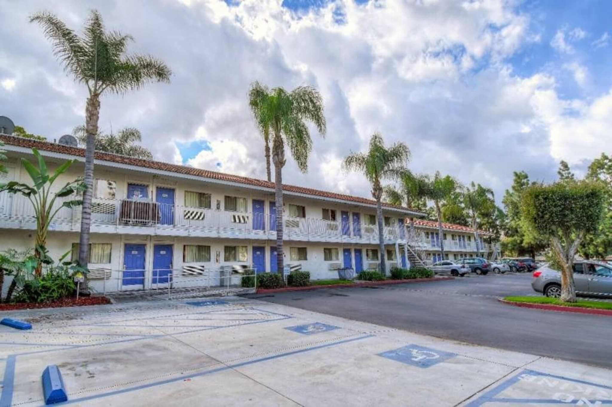 A row of motel buildings with blue doors, palm trees, and a parking lot.