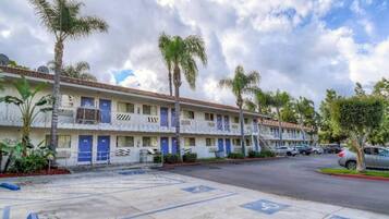A row of motel buildings with blue doors, palm trees, and a parking lot.
