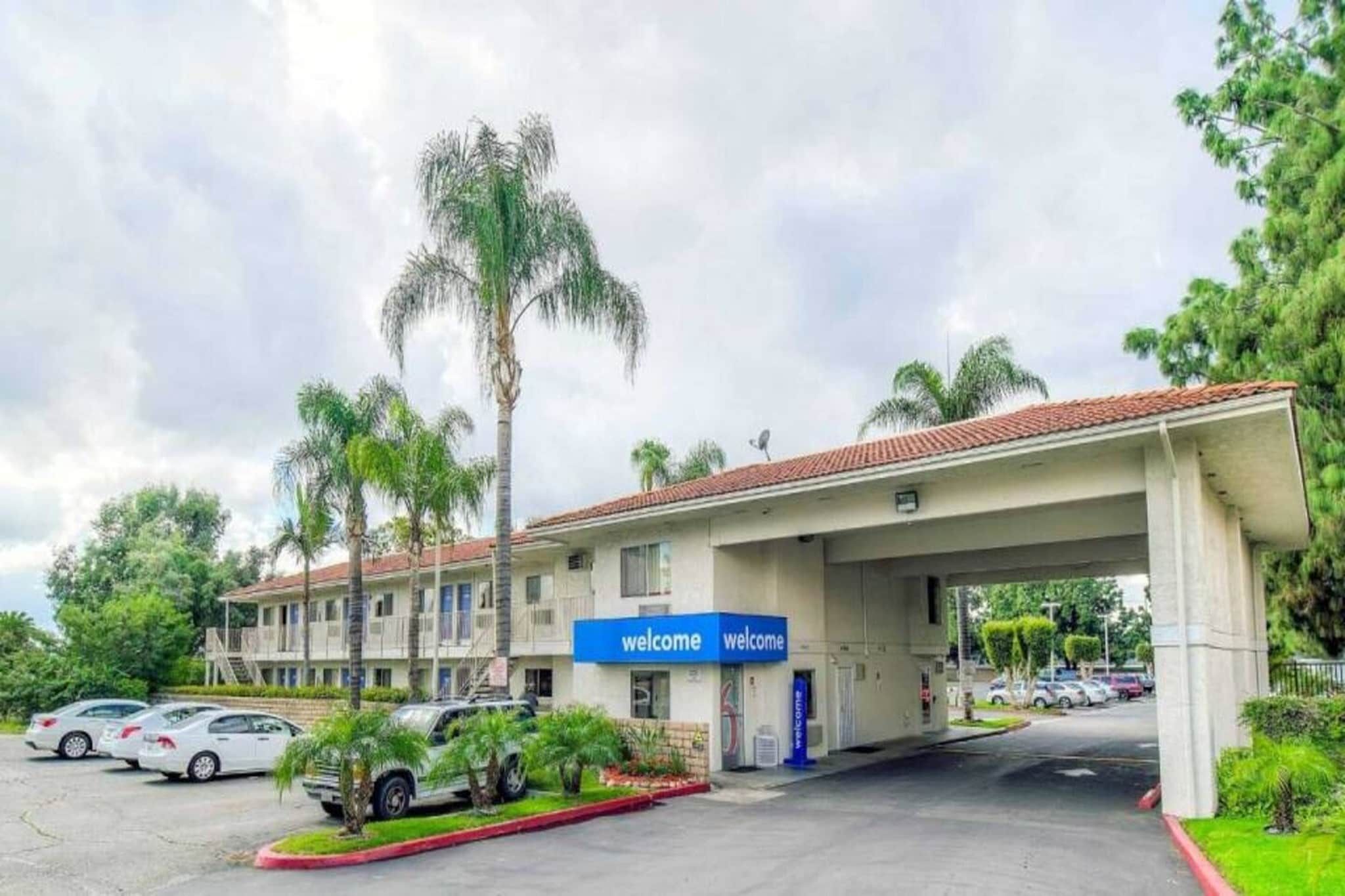 A hotel with a 'welcome' sign, a parking lot, and palm trees.
