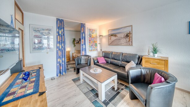 En moderne stue med sofa, lænestole, sofabord og et billede på væggen.