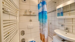 Et badeværelse med bruseforhæng, vask, spejl og et håndklædestativ.