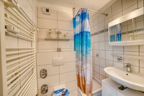 A bathroom with a shower curtain, a sink, a mirror, and a towel rack. - Vrbo Property (Heiligenhafen)