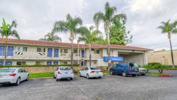 Un edificio con un letrero que dice 'welcome', varios coches estacionados adelante y palmeras.