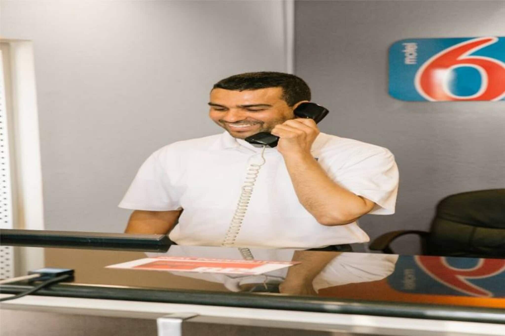 A person at a desk with a telephone, papers, and a wall with a number 6 sign.