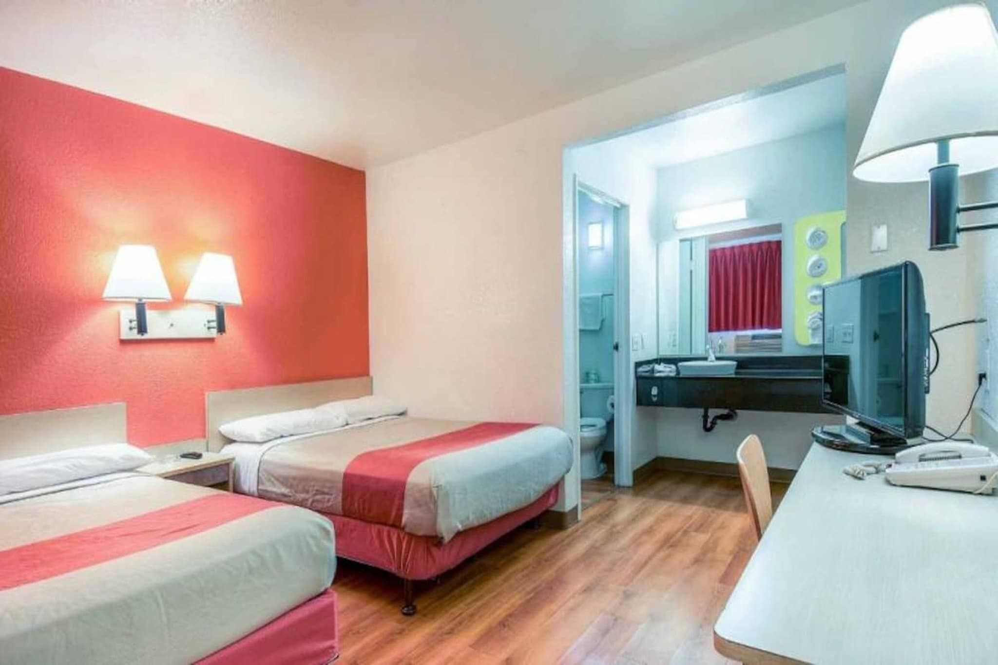 A hotel room with two beds, a desk, a television, and a bathroom visible through an open door.