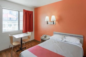 Une chambre d’hôtel avec un lit, un bureau, une chaise et une fenêtre avec des rideaux.